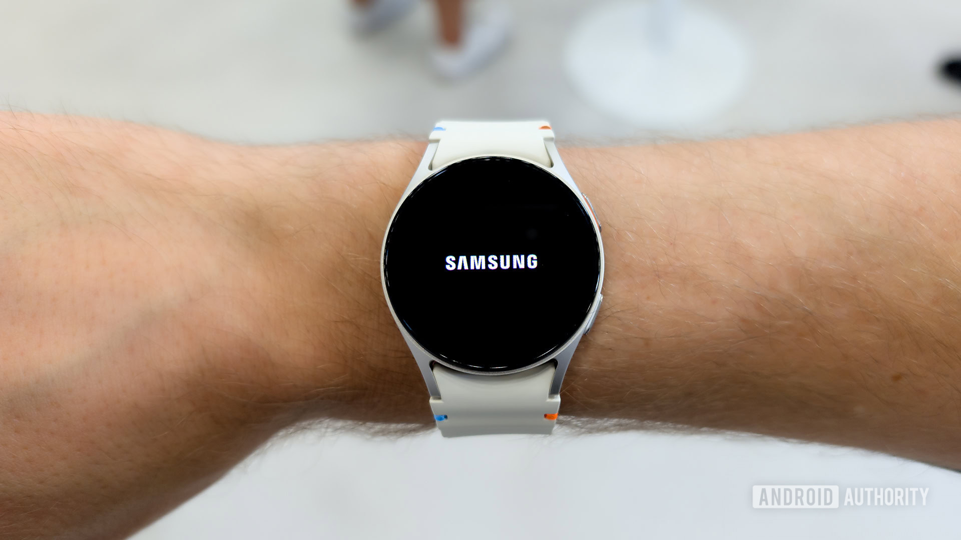 A Samsung Galaxy Watch on a male wrist displays the Samsung logo.